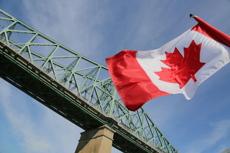 A Canadian flag flies in front of a suspension bridge