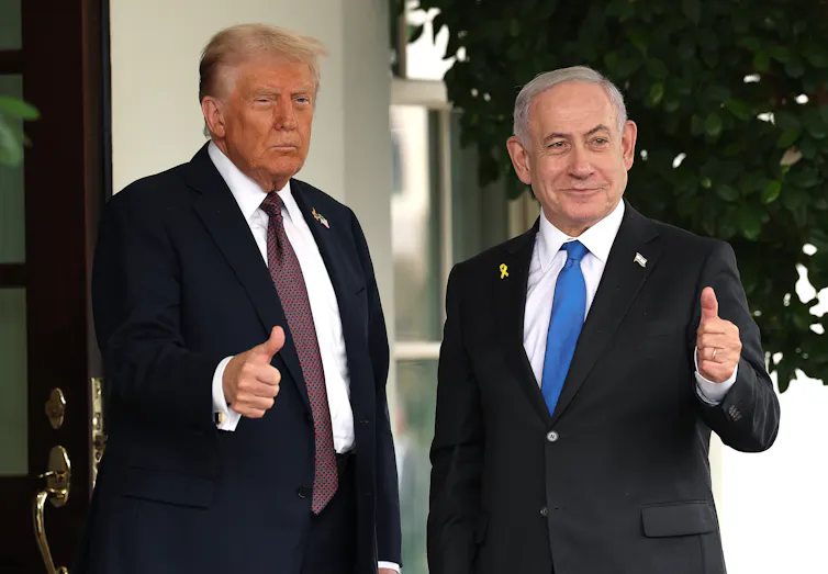 Two men in suits stand with thumbs up gestures