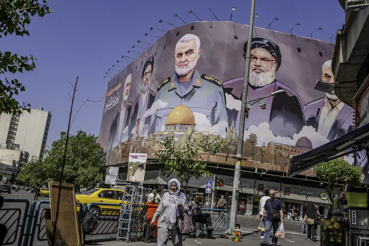 people walk on street past large billboard depicting slain anti-Israel leaders