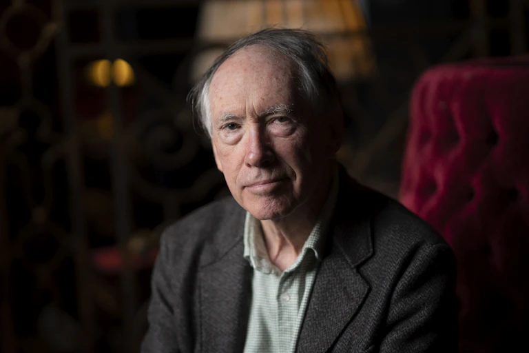Ian McEwan sitting on a red, velvet armchair.