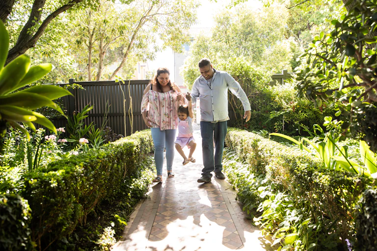 An Aboriginal mother and father swinging their young daughter down a garden path