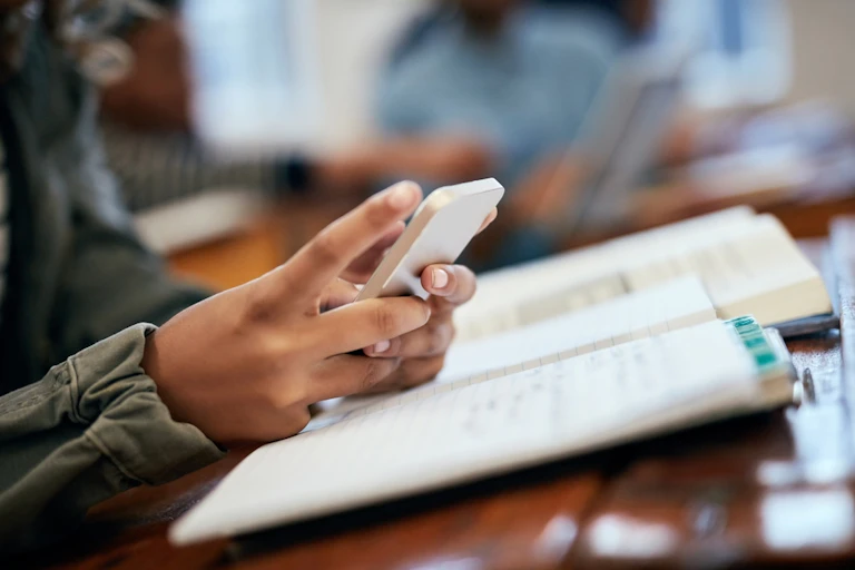 Un adolescent en train de lire un manuel et de consulter son smartphone.