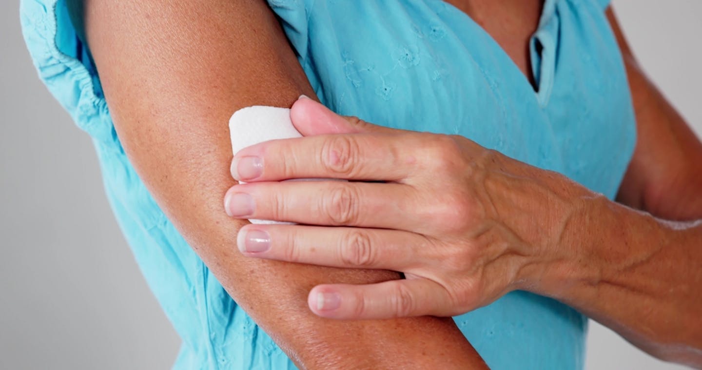 Woman putting an HRT patch on her upper arm.