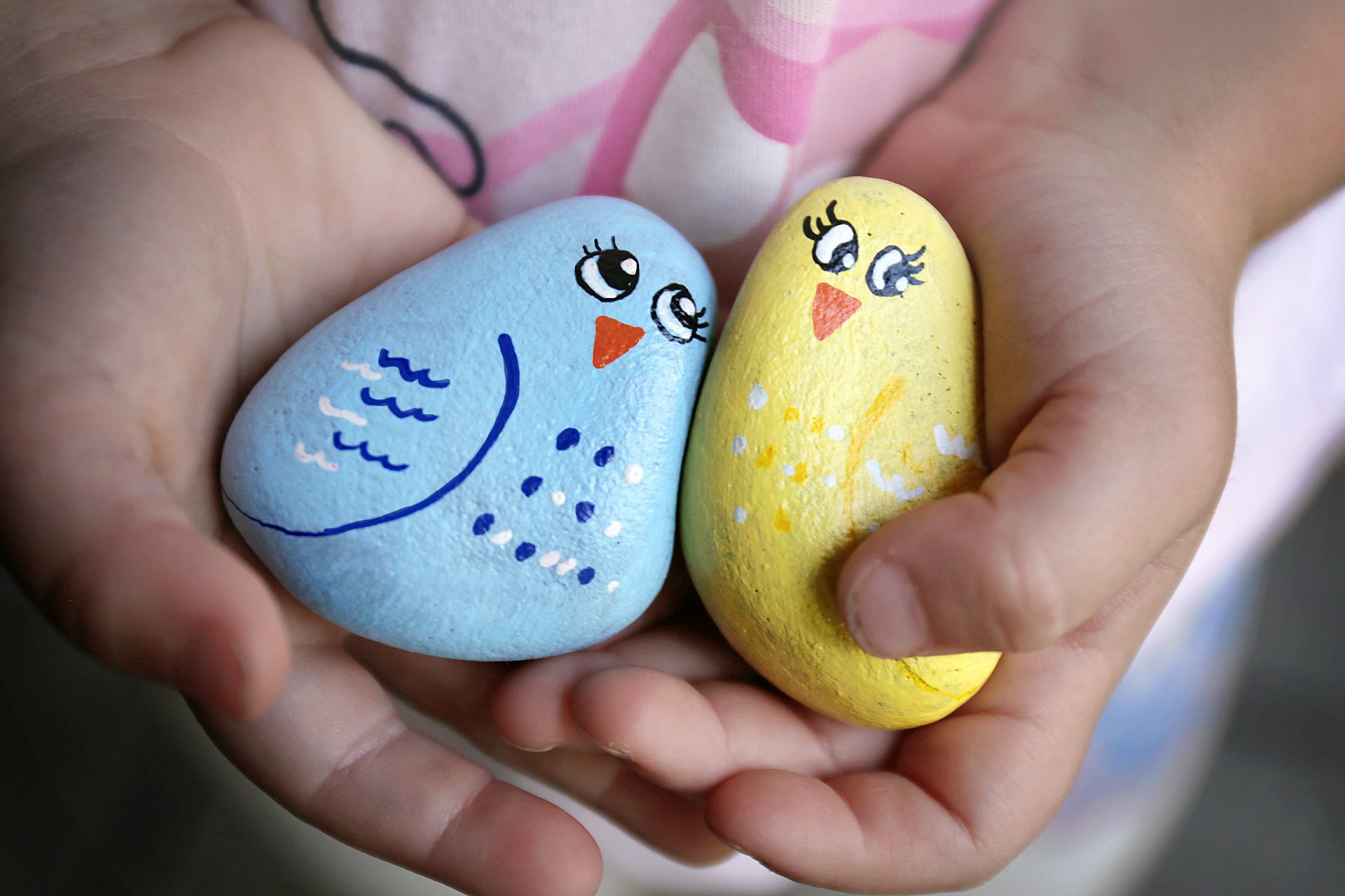The hands of a little child holding rocks painted like birds.