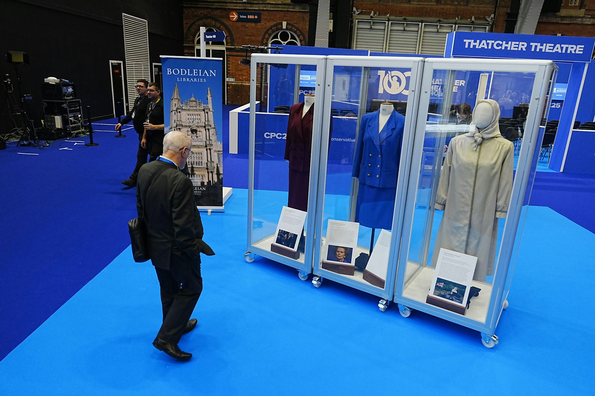 a person looking at mannequins in glass cases wearing Margaret Thatcher's clothes.