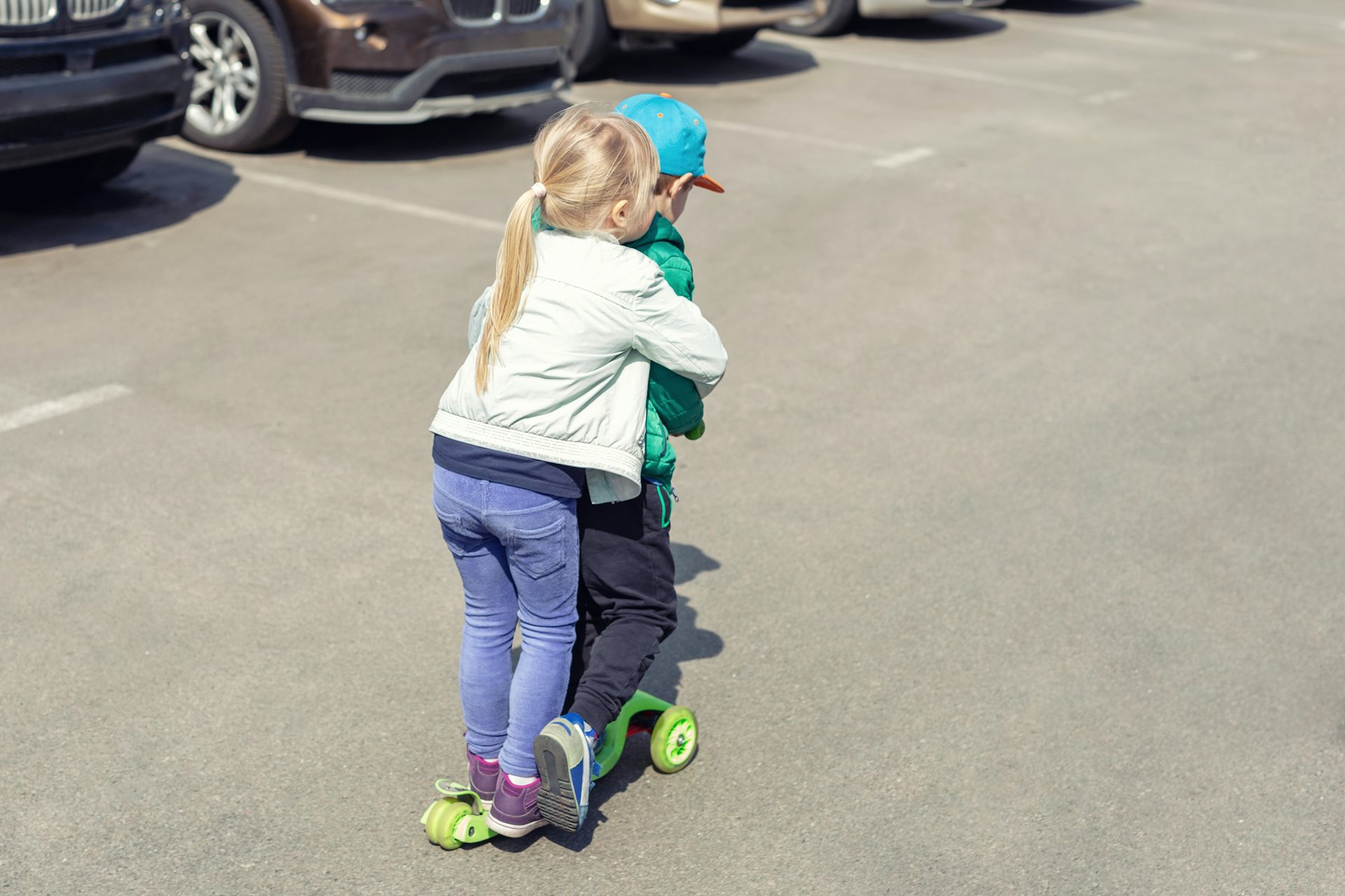 Two children on a scooter in a car park