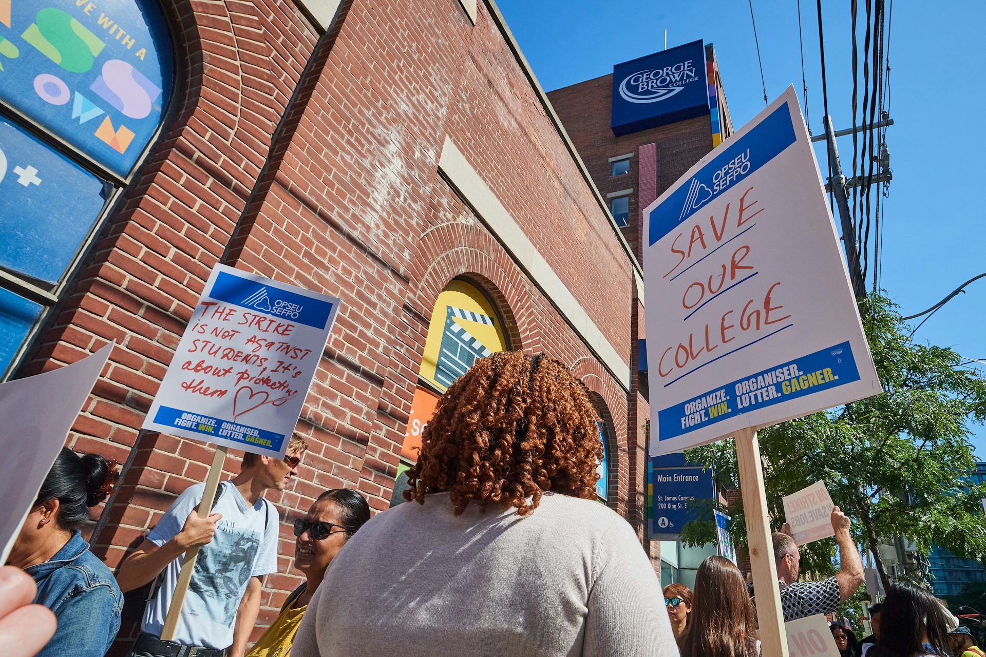 People picket on a sidewalk and one sign says save our college.