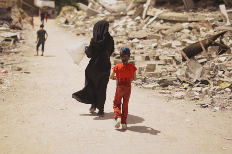 Una mujer y dos niños de espaldas entre ruinas.