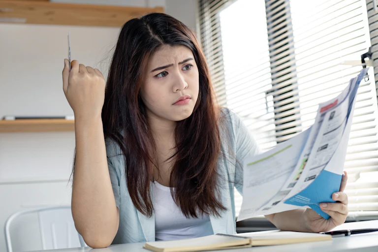 young woman looking at some paper bills with a confused expression on her face