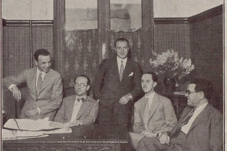 Cinco hombres posando para una foto cerca de una mesa.
