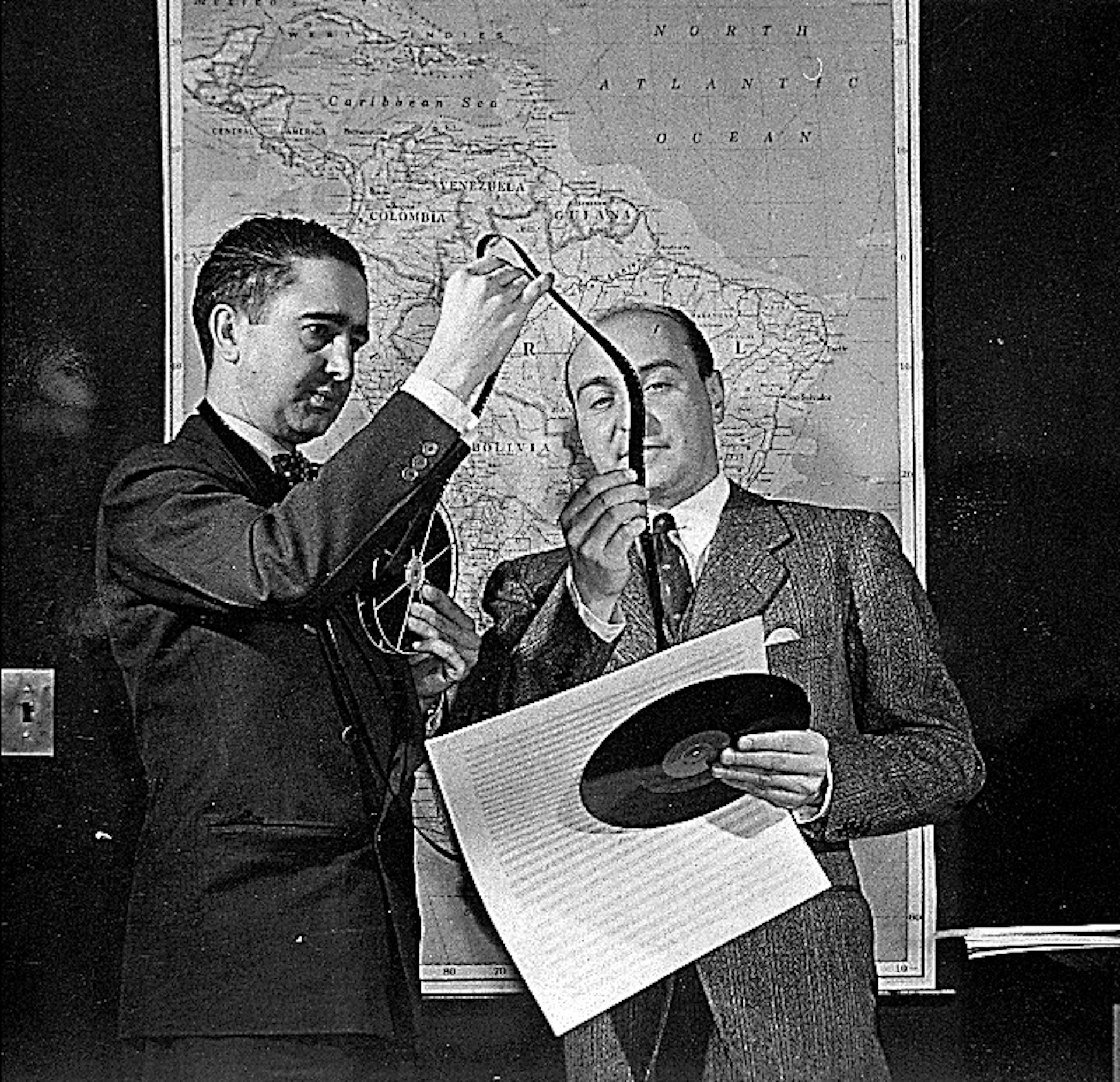 Two men watch filmmers in black and white.