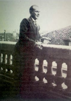 Retrato de un hombre de traje apoyado en una balaustrada.