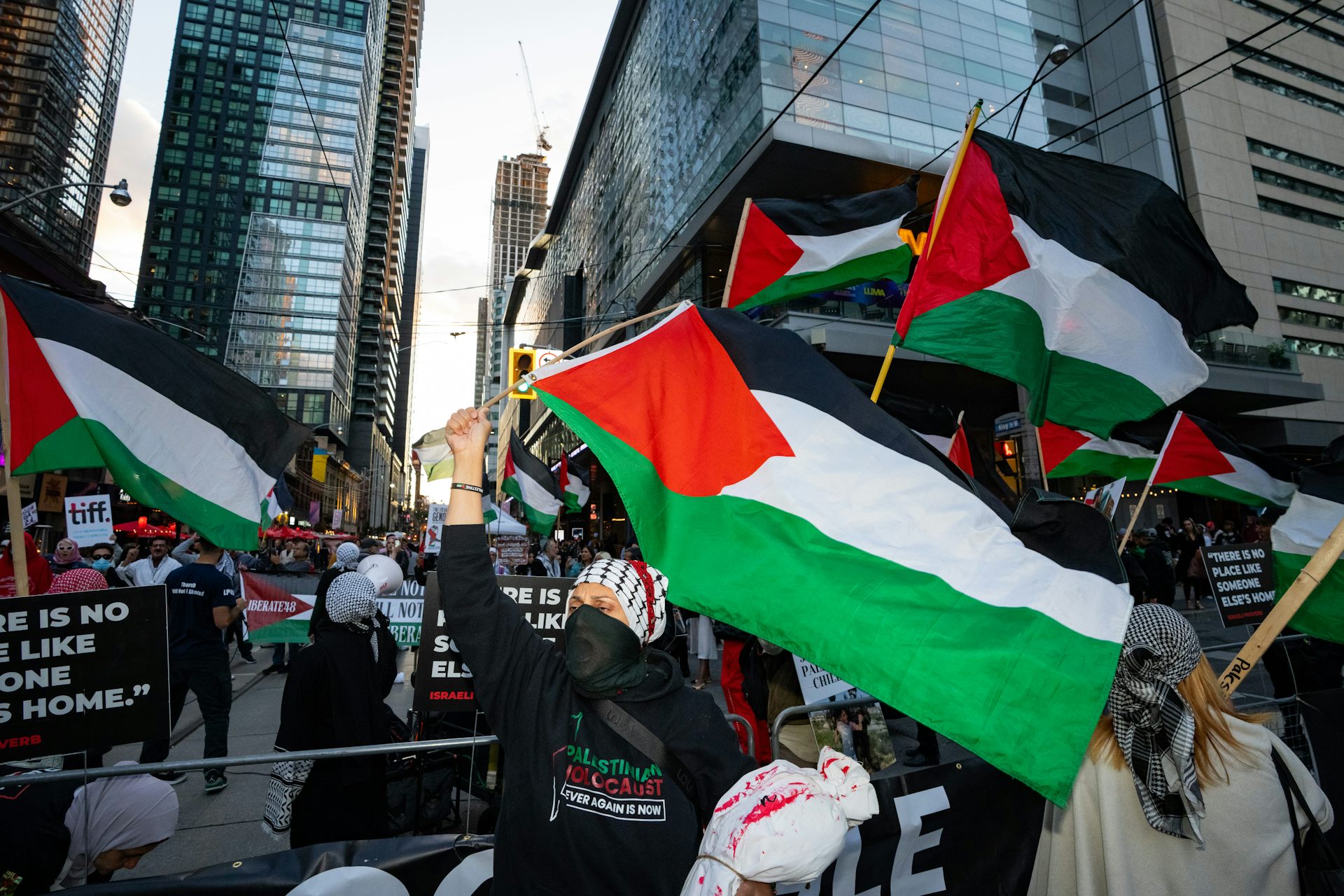 A group of protesters walking down a street waving Palestinian flags.