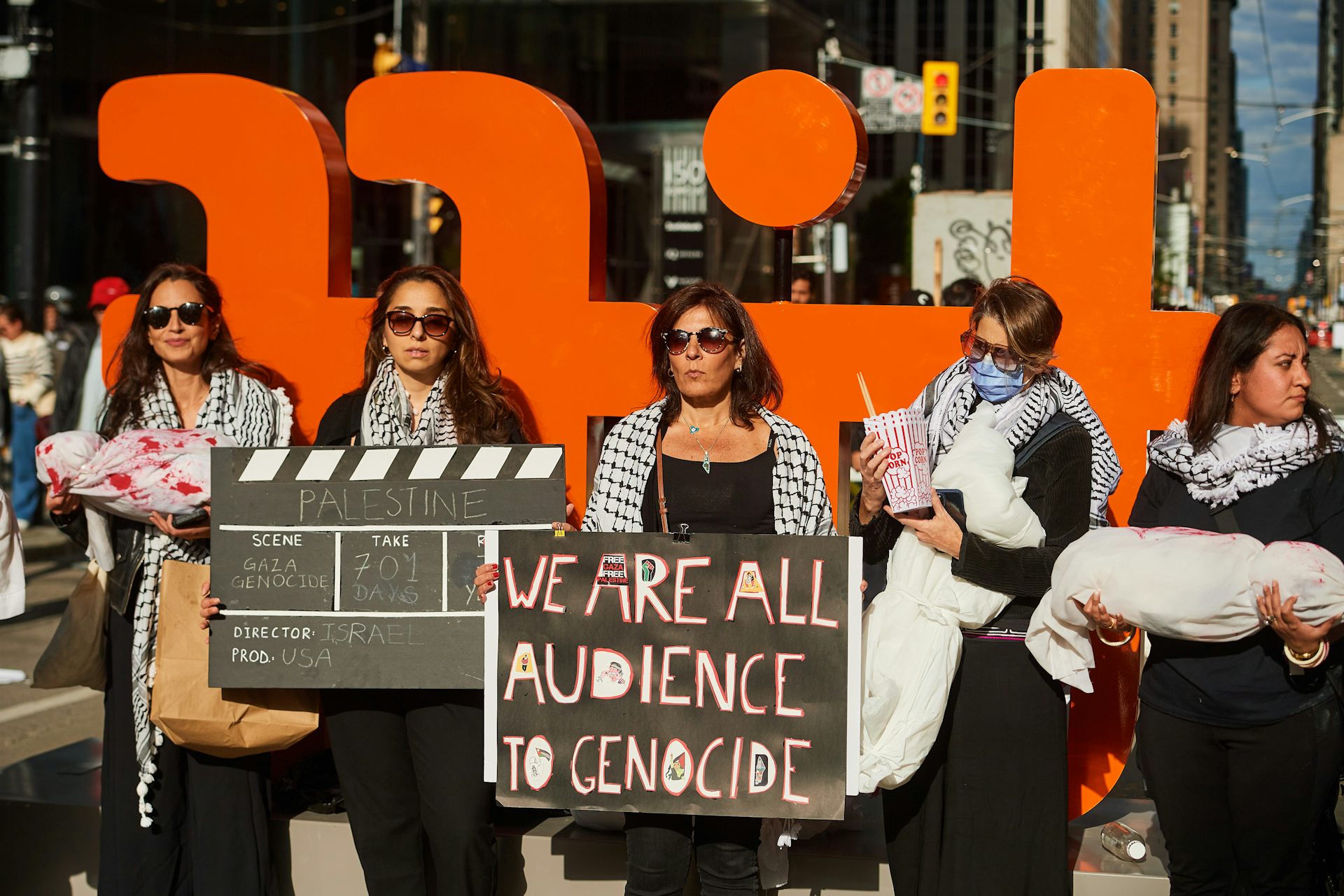 A line of protesters holding signs and standing in front of the Toronto International Film Festival sign.