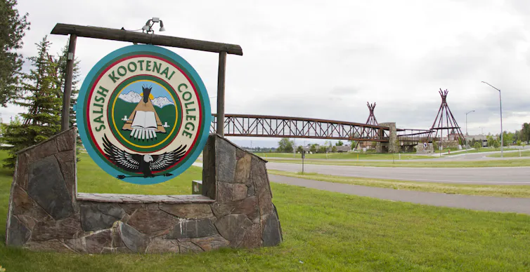 A wooden sign on a quiet road with grass says 'Salish Kootenai College.'