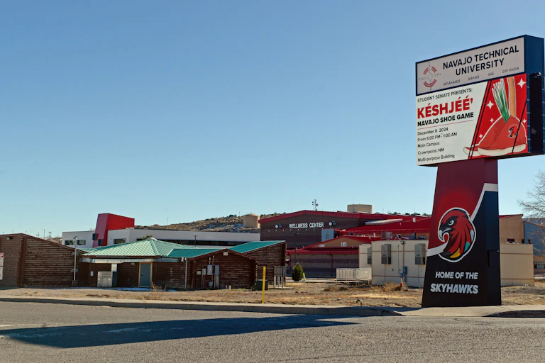 A few low-lying buildings, including one that says 'Wellness Center,' are seen with a large sign nearby that says 'Navajo Technical University'