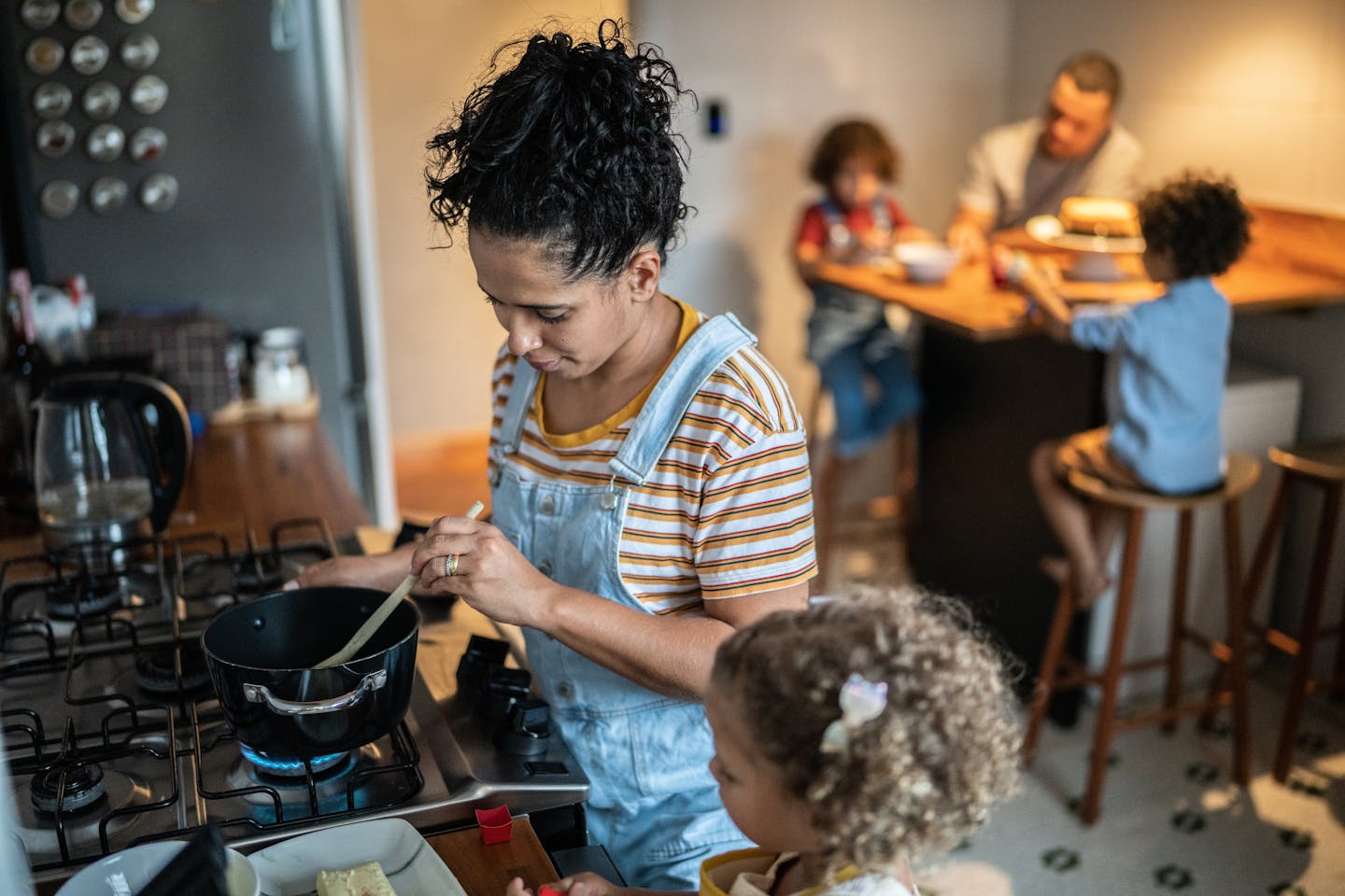Family in the kitchen, mom cooks dinner as daughter watches.