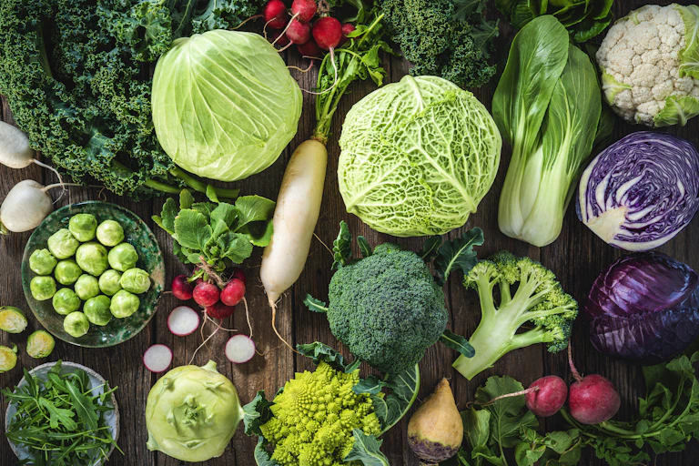 An assortment of vegetables including cabbage, broccoli, cabbage, turnip, kale, romanesco, radish, arugula, kohlrabi and swedes on wood rustic board