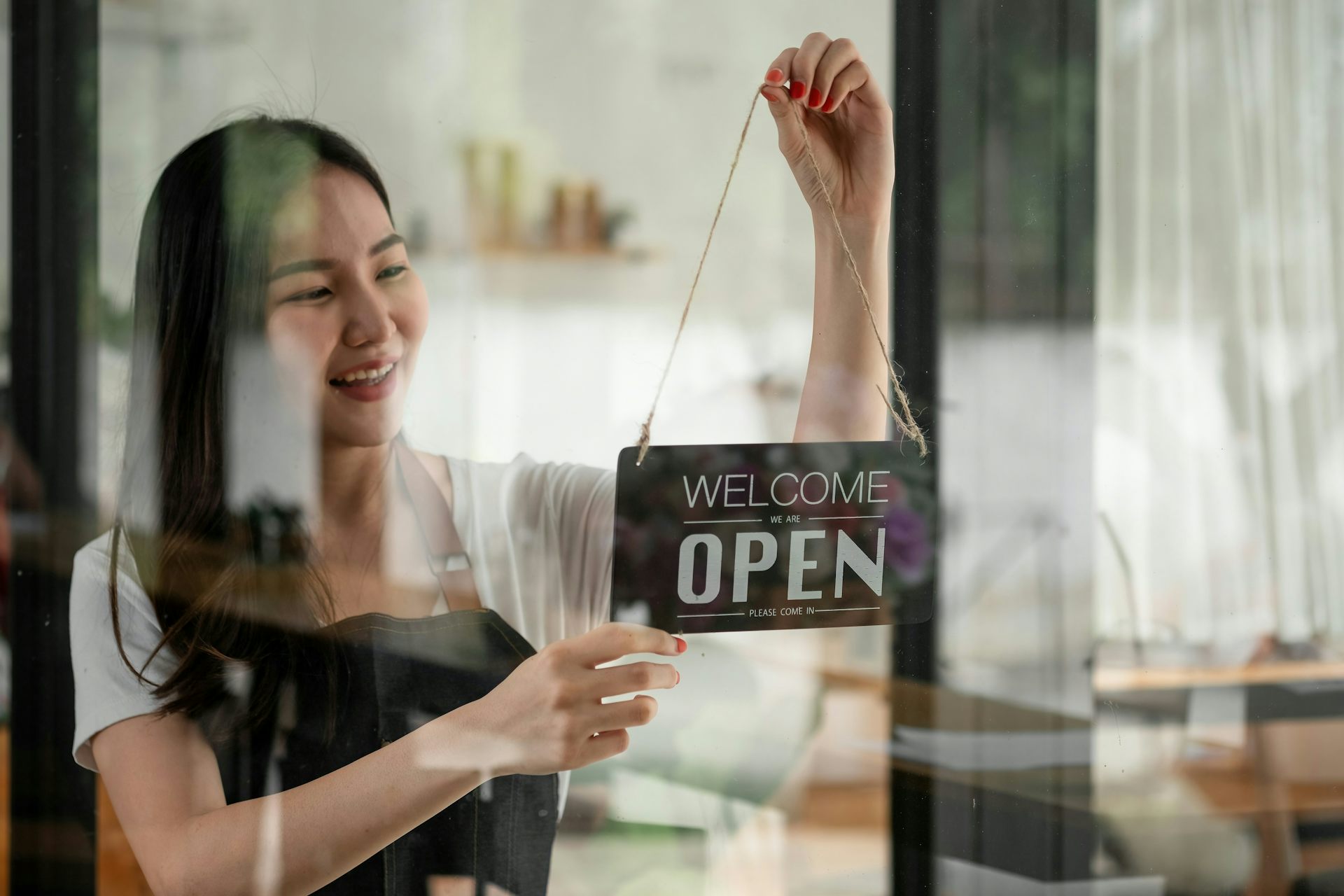 A woman hands a 'Welcome we are open' sign in the doorway of a shop