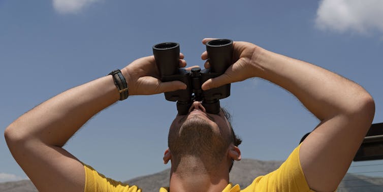 A man in a yellow top peering through bincoluars.