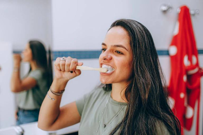 Woman in bathroom, brushing teeth, looking into mirror