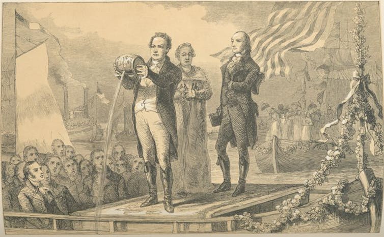 A faded black-and-white illustration of men in formal 18th-century clothing standing in front of a crowd as one pours a stream of water from a small barrel.