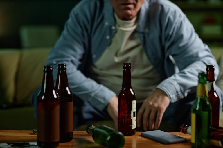 Man sits behind beer bottles strewn across a coffee table.