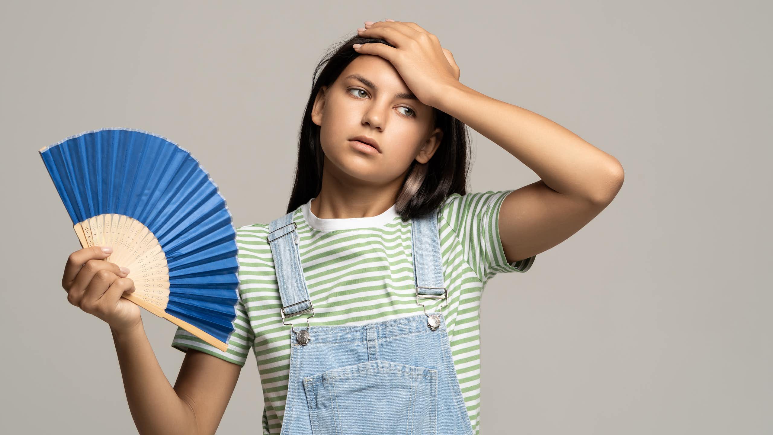 Una adolescente con un abanico hace un gesto de calor.