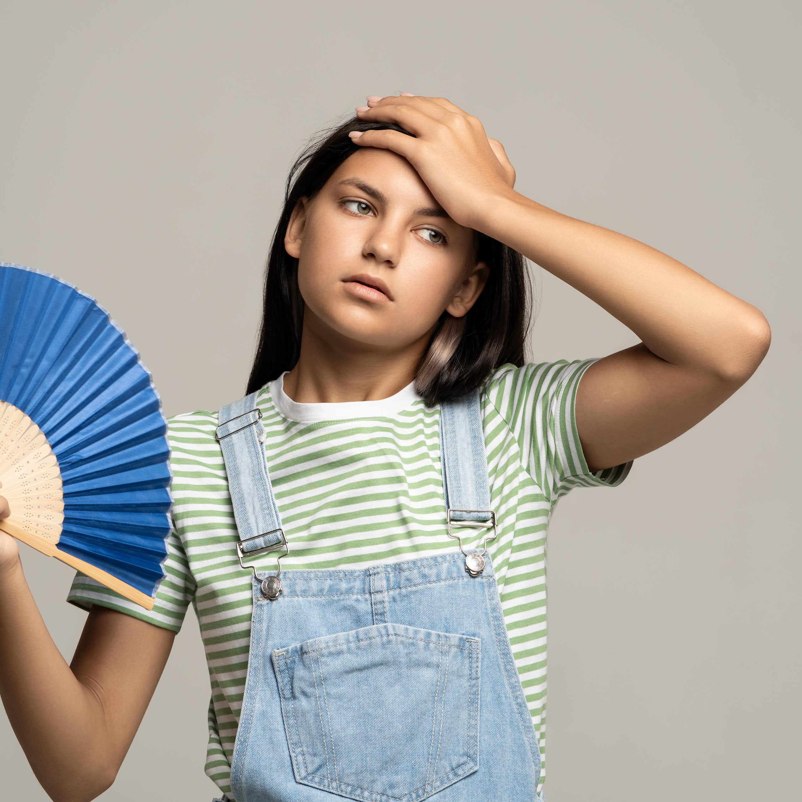 Una adolescente con un abanico hace un gesto de calor.