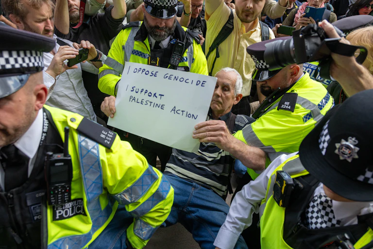 police detaining a man holding up a placard reading 'I oppose genocide, I support Palestine Action'