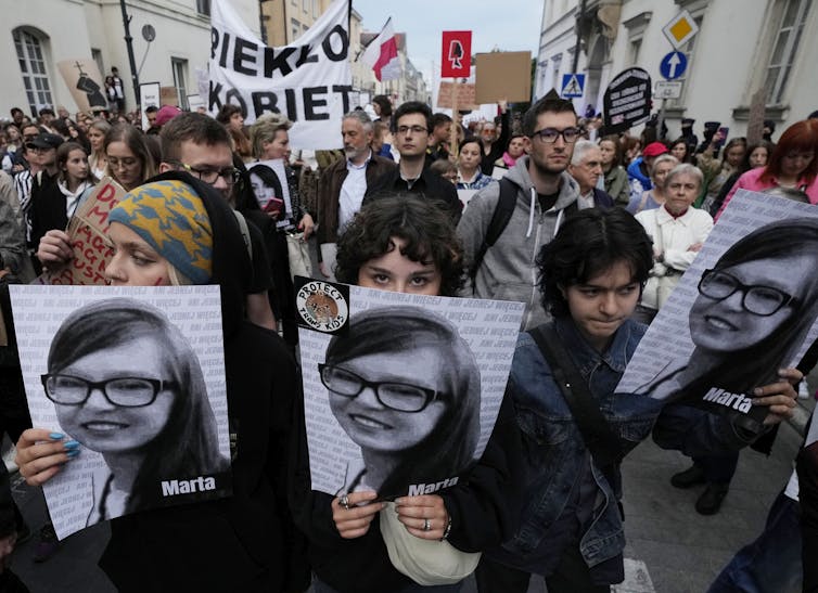 Manifestantes polacos sostienen fotografías de una mujer joven con gafas, sonriendo