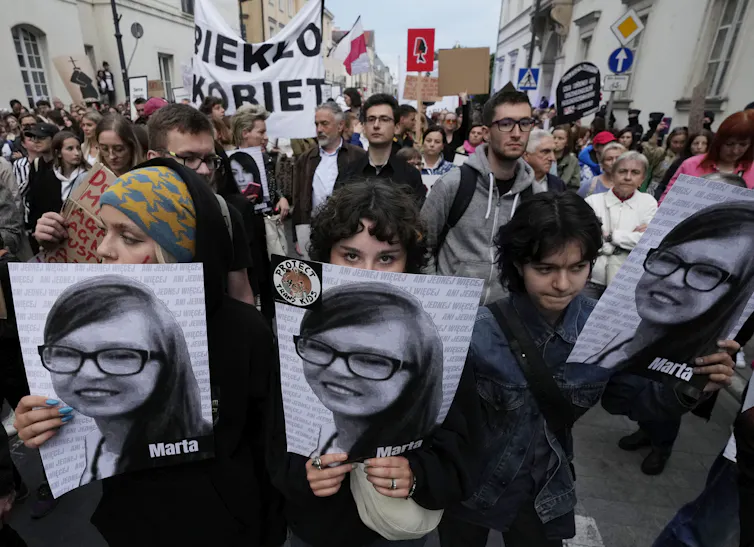 Polish protesters hold photos of a young woman with glasses, smiling