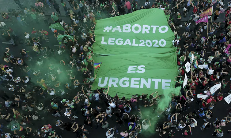 Aerial shot of a large crowd holding a banner reading 'aborto legal es urgente'