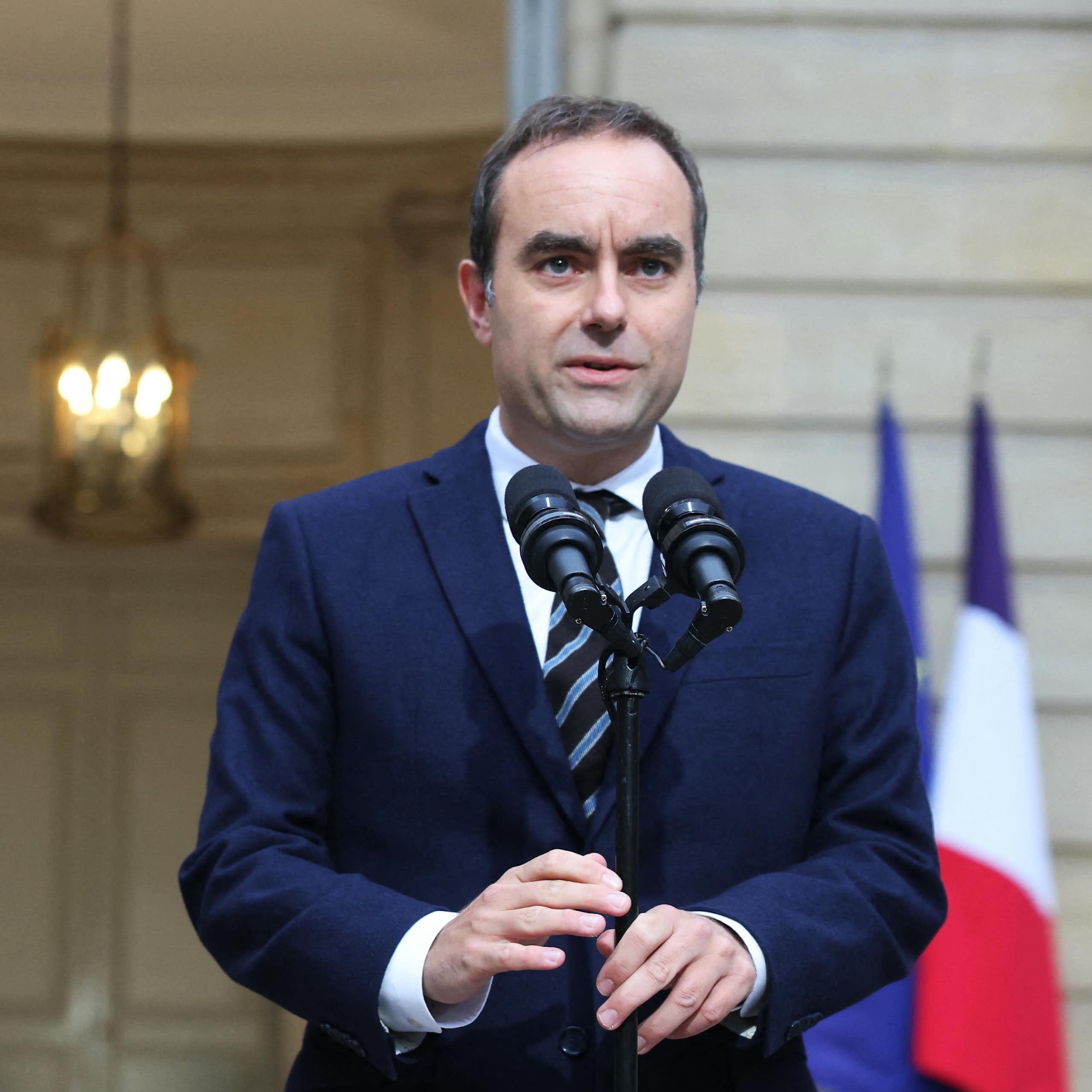 Wearing a suit and tie, French Prime Minister Sébastien Lecornu speaks in front of two microphones in daylight in front of a building.