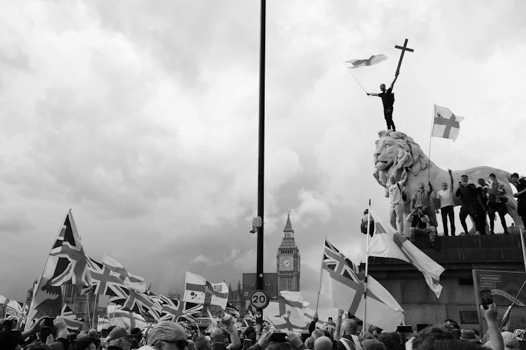 Men climbing on top of a lion sculpture waving English flags and crosses
