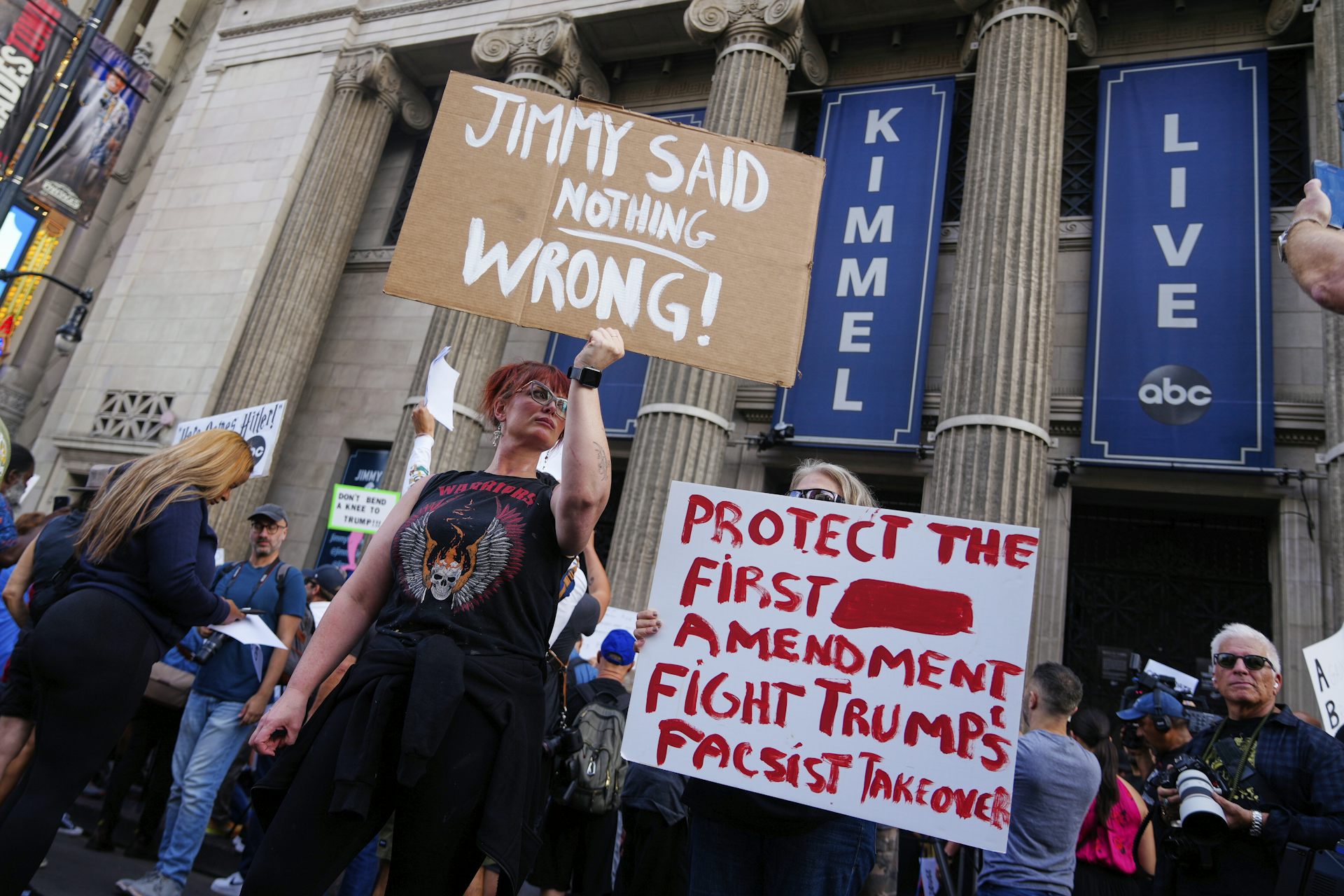 Demonstrators holds signs in front of a building with columns.