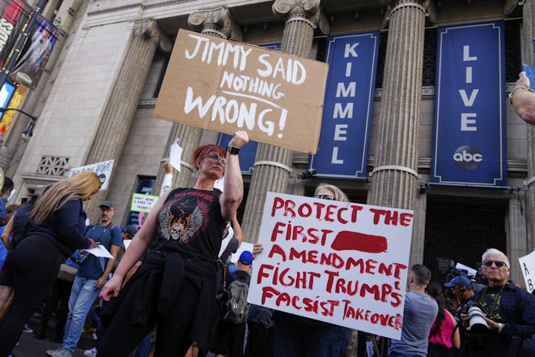 Demonstrators holds signs in front of a building with columns.