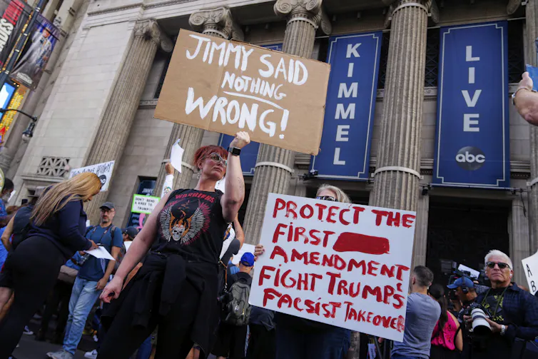 Demonstrators holds signs in front of a building with columns.