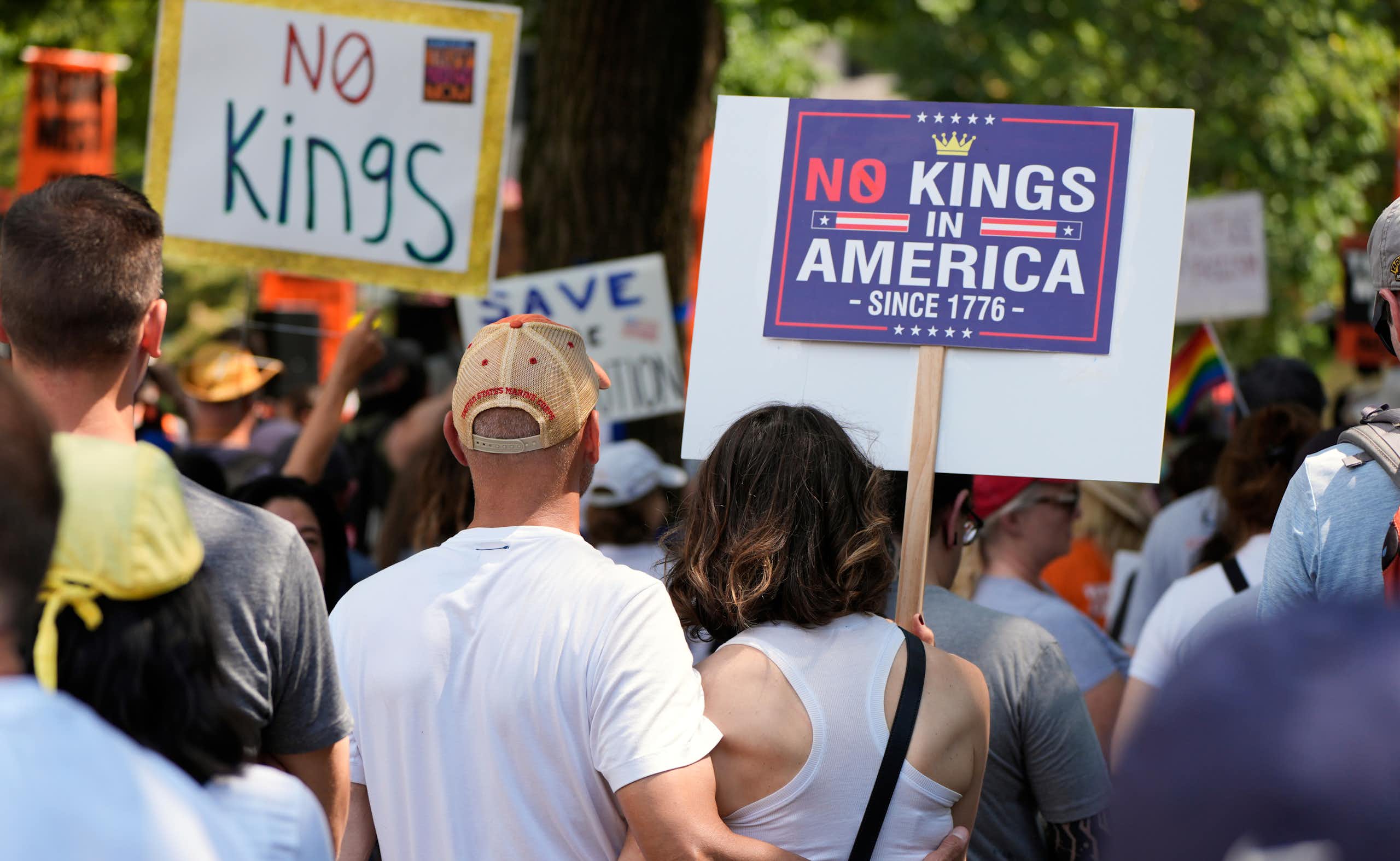 Protesters holding signs that say 'No Kings' and 'No King in America since 1776.'