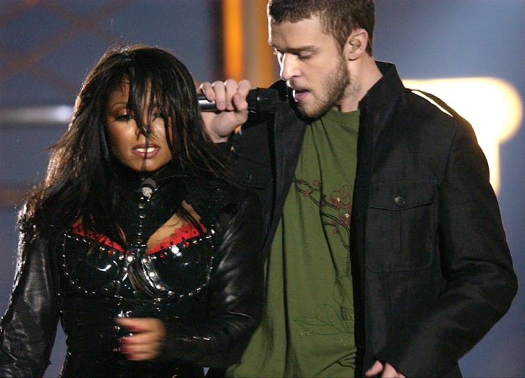 A Black woman and white man sing onstage.