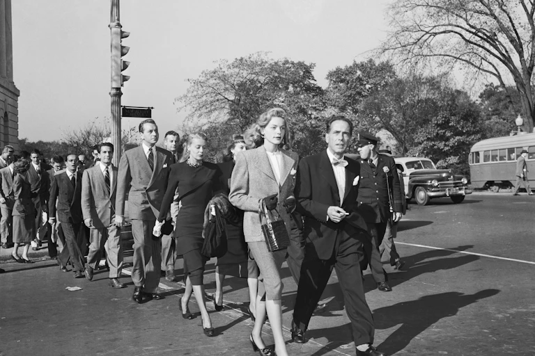 In this black and white photo of men and women in suits taken in the mid-20th century, they are walking with purpose.