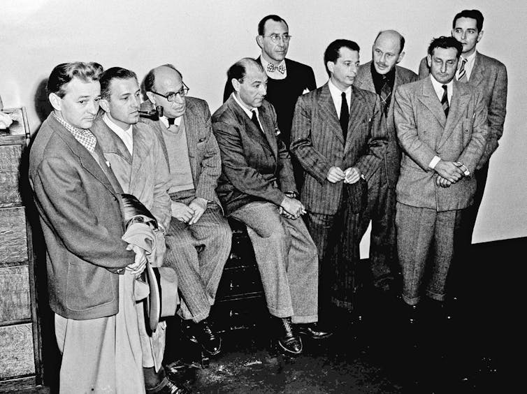 Ten men in suits stand together in a black-and-white photograph taken in the mid-20th century.