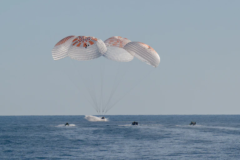 A spacecraft splashing into the ocean, attached to three parachutes.