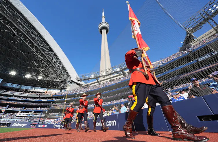 Mountrie en Red Coat Series lleva una bandera canadiense con montañas detrás de él y una torre CN que juega sobre él.