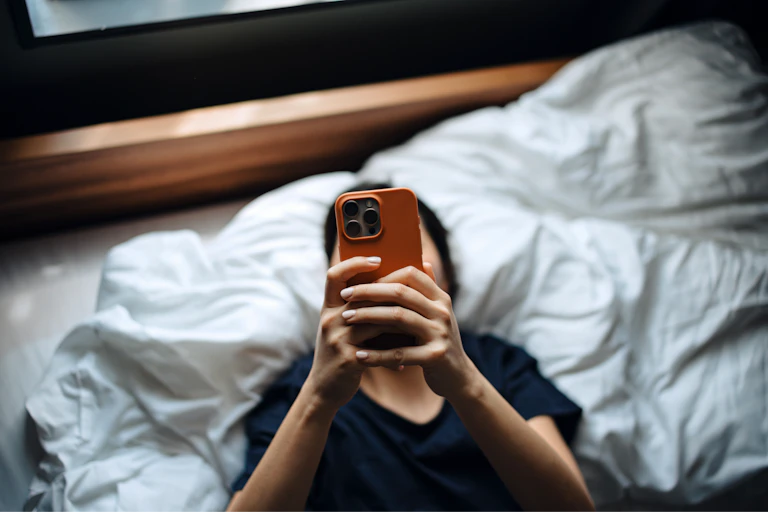 Woman looks at smartphone in bed