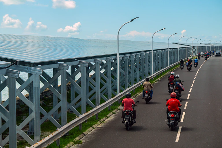 people riding mopeds past a solar array on highway.