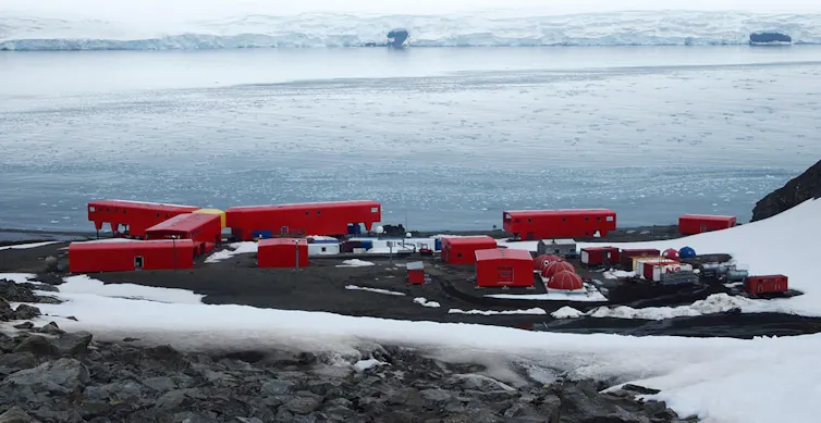 Un conjunto de construcciones rojas sobre un terreno cubierto de nieve y al fondo el mar helado