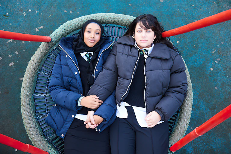 Two girls lying on a swing in a park