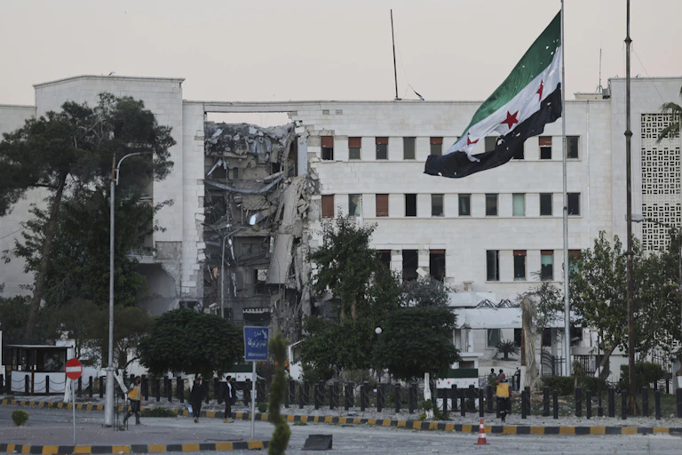 A flag is seen in front of a damaged building.