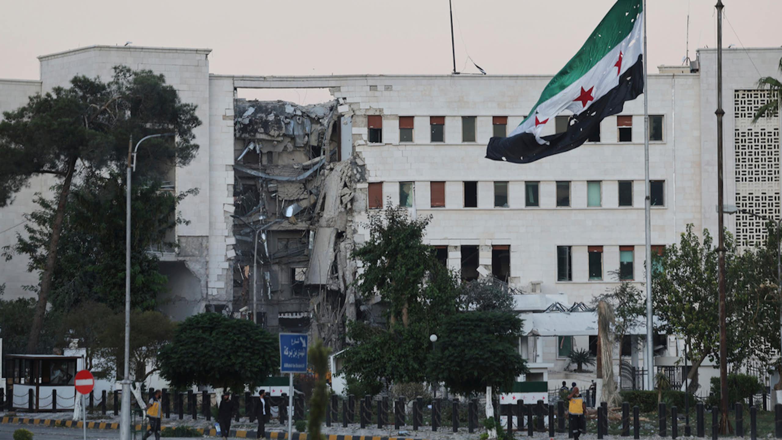 A flag is seen in front of a damaged building.